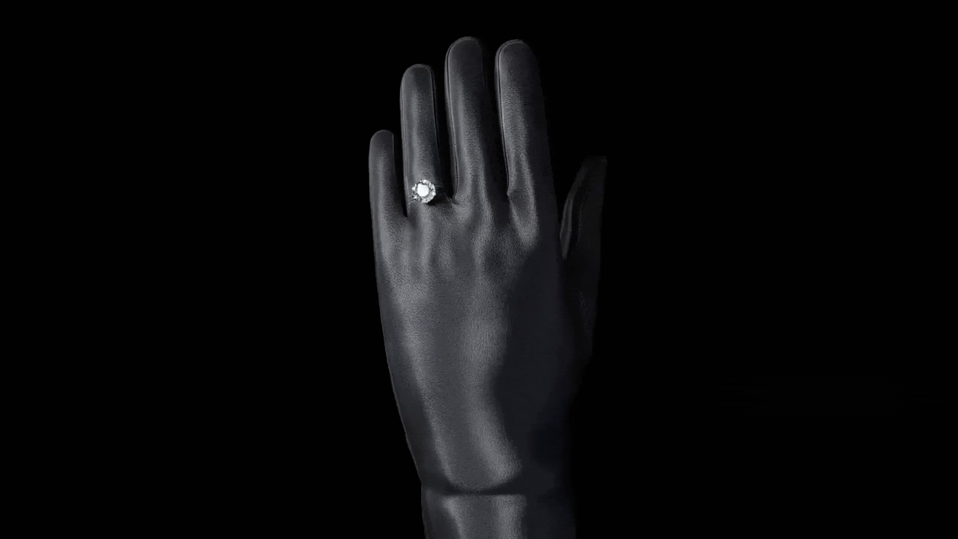 Rotating animated gif of a black left handed glove with a People's diamond ring on the ring finger glistening, protruding through a slit in the glove.