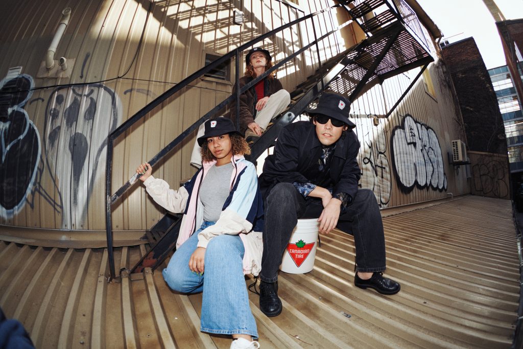 3 people wearing bucket hats posing at the bottom of a fire escape.